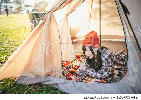 A woman using her smartphone while sleeping in a tent at a campsite 120409449