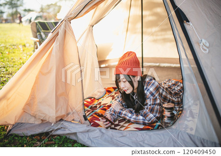 A woman using her smartphone while sleeping in a tent at a campsite 120409450