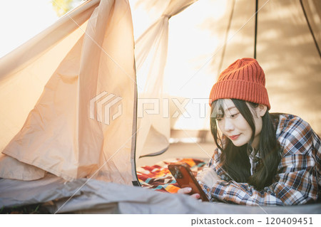 一位女士在露營時睡在帳篷裡玩智慧型手機 120409451