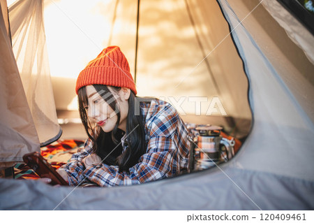 A woman using her smartphone while sleeping in a tent at a campsite 120409461