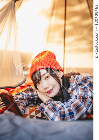 A woman using her smartphone while sleeping in a tent at a campsite A woman using her smartphone while sleeping in a tent at a campsite 120409465