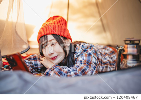 A woman using her smartphone while sleeping in a tent at a campsite 120409467