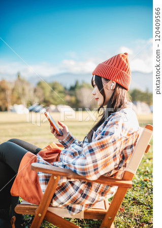 Woman sitting at a campsite and listening to music Woman sitting at a campsite and listening to music 120409566