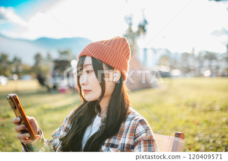 Woman sitting at a campsite and listening to music Woman sitting at a campsite and listening to music 120409571
