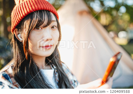 Woman sitting at a campsite and listening to music 120409588