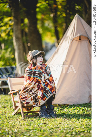 A woman drinking a drink while wrapped in a blanket at a campsite 120409699