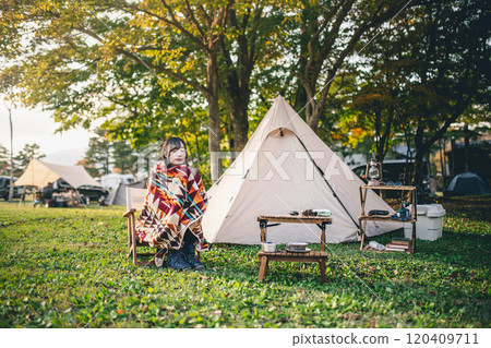 A woman drinking a drink while wrapped in a blanket at a campsite A woman drinking a drink while wrapped in a blanket at a campsite 120409711