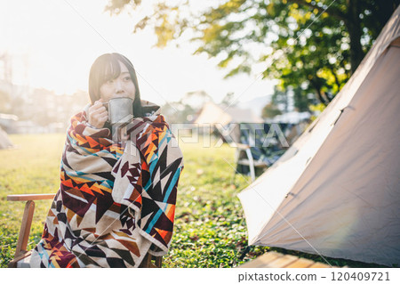 一名婦女在露營地裹著毯子喝飲料 120409721