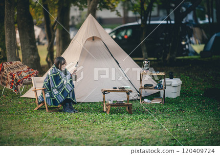 一名婦女在露營地裹著毯子喝飲料 一名婦女在露營地裹著毯子喝飲料 120409724