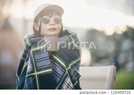 一名婦女在露營地裹著毯子喝飲料 一名婦女在露營地裹著毯子喝飲料 120409726