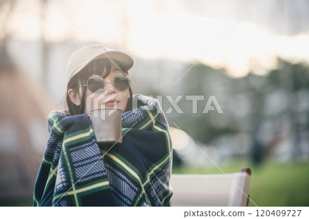 一名婦女在露營地裹著毯子喝飲料 120409727
