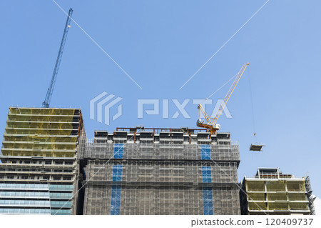 Low-angle view of cranes and steel structures of building construction with a blue sky background. Low-angle view of cranes and steel structures of building construction with a blue sky background. 120409737