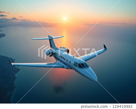 Private jet flying over ocean during sunset with vibrant sky and calm waters in the background 120410982
