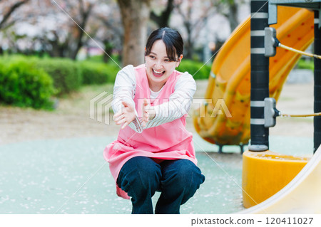A nursery teacher playing with a child in front of the playground equipment 120411027