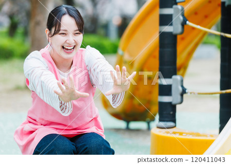 A nursery teacher playing with a child in front of the playground equipment 120411043