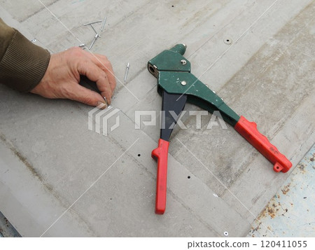 riveting tool on iron texture top view and male hand holding aluminum rivet, hand held device for setting rivets when joining thin metal parts riveting tool on iron texture top view and male hand holding aluminum rivet, hand held device for setting rivets when joining thin metal parts 120411055