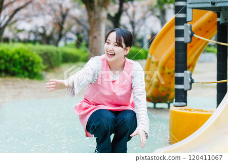 A nursery teacher playing with a child in front of the playground equipment 120411067