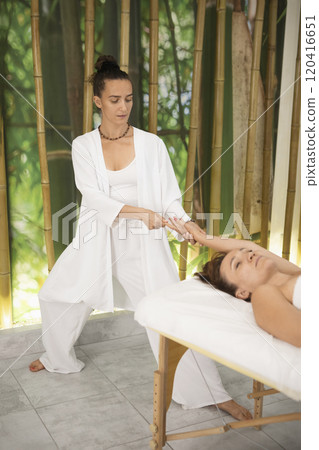Beautiful female manual physician works with woman who lying on back on massage table in pro salon, vertical image, selective focus. 120416651