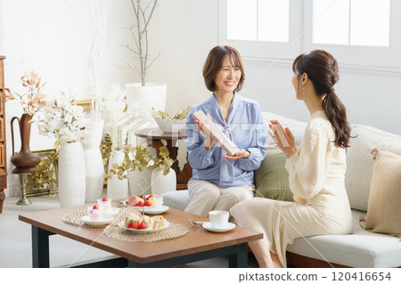 A daughter in her 30s giving a gift and her mother receiving it in a hotel tea room 120416654