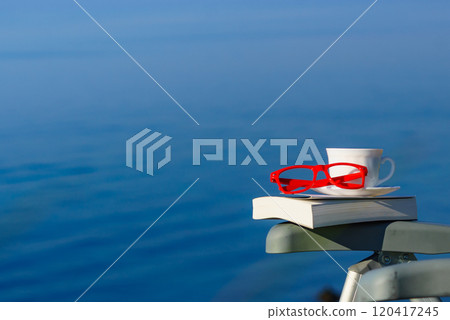 Coffee cup, book and glasses against blue sea. 120417245