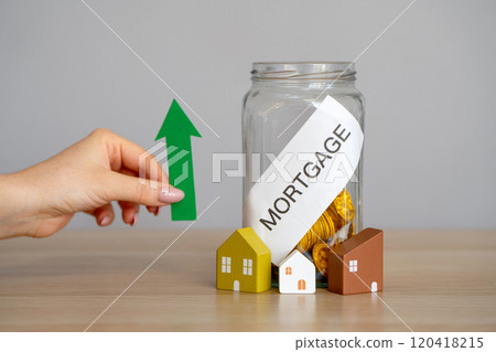Raising mortgage rate and increase in interest charges. Loan for housing, real estate. Glass jar with coins, houses and an arrow pointing up. Raising mortgage rate and increase in interest charges. Loan for housing, real estate. Glass jar with coins, houses and an arrow pointing up. 120418215