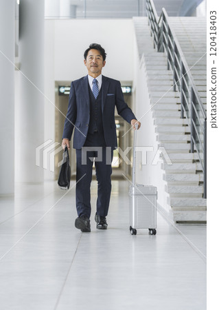 Image of a businessman on a business trip: A businessman in his 50s walking with a suitcase and business bag Image of a businessman on a business trip: A businessman in his 50s walking with a suitcase and business bag 120418403