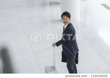 A businessman in his 50s walking with a suitcase and a business bag 120418426