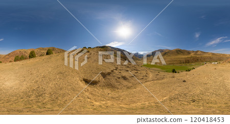 Spherical HDRi panorama of dry dust covered hill in mountains with blue sky and sun above. 120418453