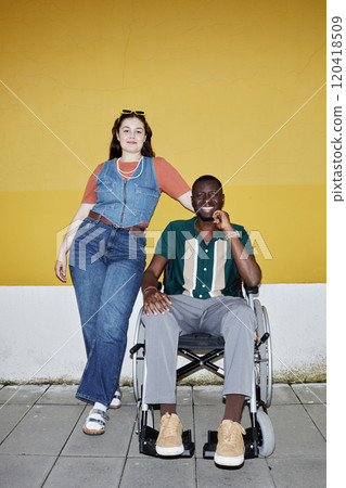 Vertical full length portrait of young African American man using wheelchair posing with friend or partner against yellow wall in city shot with flash 120418509