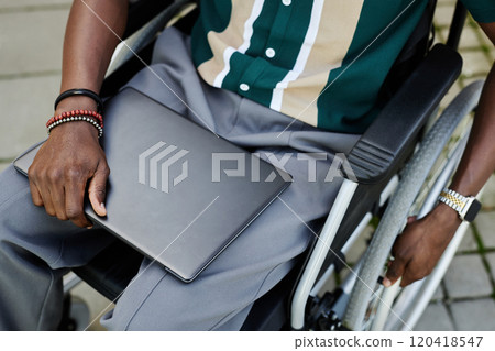 Top view closeup of unrecognizable African American man with disability holding laptop and sitting in wheelchair copy space Top view closeup of unrecognizable African American man with disability holding laptop and sitting in wheelchair copy space 120418547