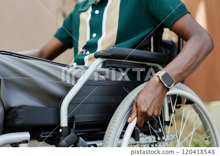 Close up of African American man using wheelchair while moving in city outdoors with focus on hands on wheel and smartwatch copy space Close up of African American man using wheelchair while moving in city outdoors with focus on hands on wheel and smartwatch copy space 120418548