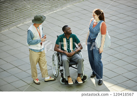 Minimal high angle shot of diverse group of friends with African American man using wheelchair smiling happily and chatting in city outdoors 120418567