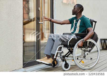 Side view full length portrait of adult African American man with disability using wheelchair and opening door in city copy space Side view full length portrait of adult African American man with disability using wheelchair and opening door in city copy space 120418568