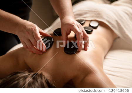 A massage therapist places hot stones on a client's back during a stone therapy session. Hot stone massage concept A massage therapist places hot stones on a client's back during a stone therapy session. Hot stone massage concept 120418606