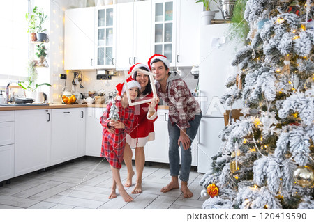 Happy family in santa hats with tiny house in cozy home with Christmas decor of festive white kitchen. Gift for New Year. Insurance, moving to new house, mortgage, rent and purchase real estate Happy family in santa hats with tiny house in cozy home with Christmas decor of festive white kitchen. Gift for New Year. Insurance, moving to new house, mortgage, rent and purchase real estate 120419590