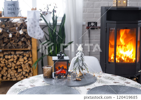 Metall black stove, burning hearth fireplace in white Festive interior of house is decorated for Christmas and New Year, Christmas tree. firewood in the woodpile, cozy and heating of home 120419685
