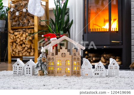 Key on Christmas tree and tiny house on cozy home with Christmas decor near the burning stove fireplace. Gift for New Year. Insurance, moving to new house, mortgage, rent and real estate 120419696