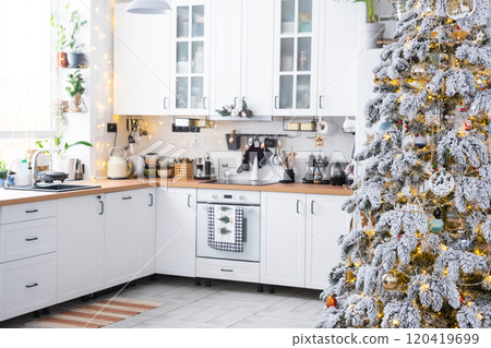 Festive Christmas decor in white kitchen, modern rustic interior with a snowy Christmas tree and fairy lights. New Year, Christmas mood, cozy home. The general plan 120419699