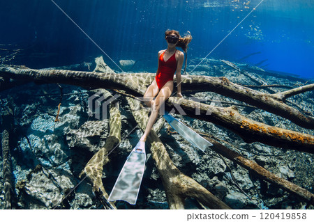 Woman free diver posing underwater on sunken log in crystal-clear lake. Freediving in fresh water lake in Indonesia 120419858