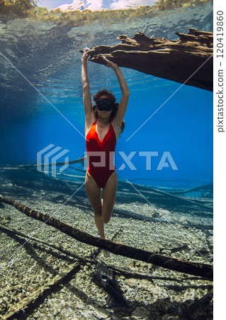 Woman free diver posing underwater with sunken logs at the bottom of the lake. Freediving in crystal-clear lake 120419860