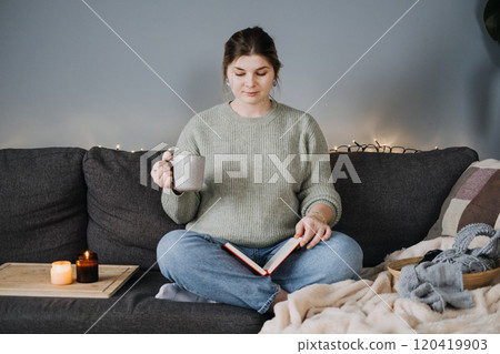 Pregnant woman enjoying a warm drink and book on cozy sofa. Autumn Winter comfort, self-care, and seasonal relaxation. Pregnant woman enjoying a warm drink and book on cozy sofa. Autumn Winter comfort, self-care, and seasonal relaxation. 120419903