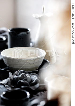 Rustic table setting with empty craft handmade ceramic tableware, black and white rough bowls, cups, jug and vase on linen tablecloth. Dry reed flowers. Day light dining room. Rustic table setting with empty craft handmade ceramic tableware, black and white rough bowls, cups, jug and vase on linen tablecloth. Dry reed flowers. Day light dining room. 120420099