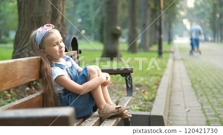Small irritated child girl sitting alone on a bench in summer park. Small irritated child girl sitting alone on a bench in summer park. 120421730