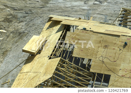 Professional builders working on roof construction of unfinished suburban home with wooden frame structure in Florida rural area. Concept of housing development in America Professional builders working on roof construction of unfinished suburban home with wooden frame structure in Florida rural area. Concept of housing development in America 120421769