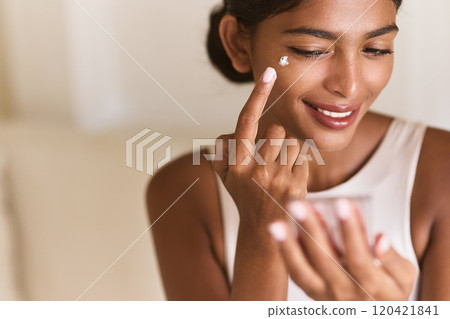 Smiling Woman Applying Moisturizer Cream to Her Face at Home 120421841