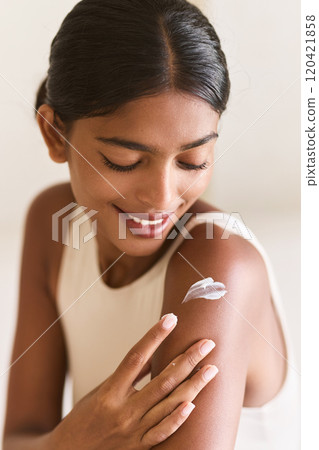 Smiling Woman Applying Moisturizing Cream to Skin for Softness and Glow 120421858