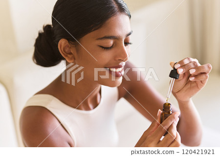 Woman Enjoying Aromatherapy With Essential Oil Dropper in Soft Light 120421921