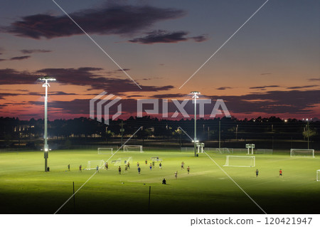 Illuminated public sports arena in North Port, Florida with people playing soccer game on grass football stadium at sunset. Outdoor activities concept Illuminated public sports arena in North Port, Florida with people playing soccer game on grass football stadium at sunset. Outdoor activities concept 120421947