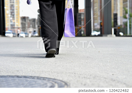 Woman crossing street with purple shopping bag in casual black outfit on a crosswalk. Woman crossing street with purple shopping bag in casual black outfit on a crosswalk. 120422482