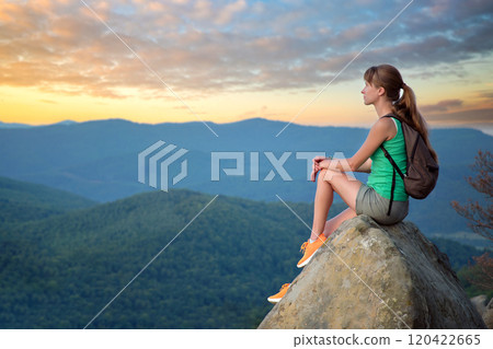 Hiker girl resting on rocky mountain top enjoying morning nature during her travel on wilderness trail. Lonely female traveler traversing high hilltop route. Healthy lifestyle concept 120422665